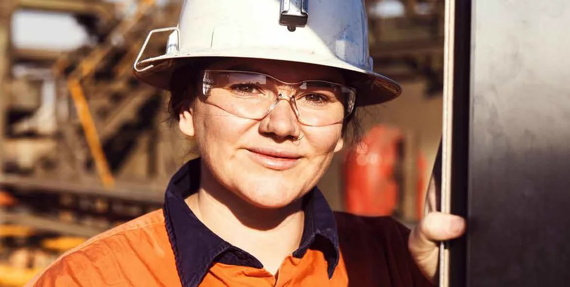 A smiling worker in a hard hat and safety glasses on site