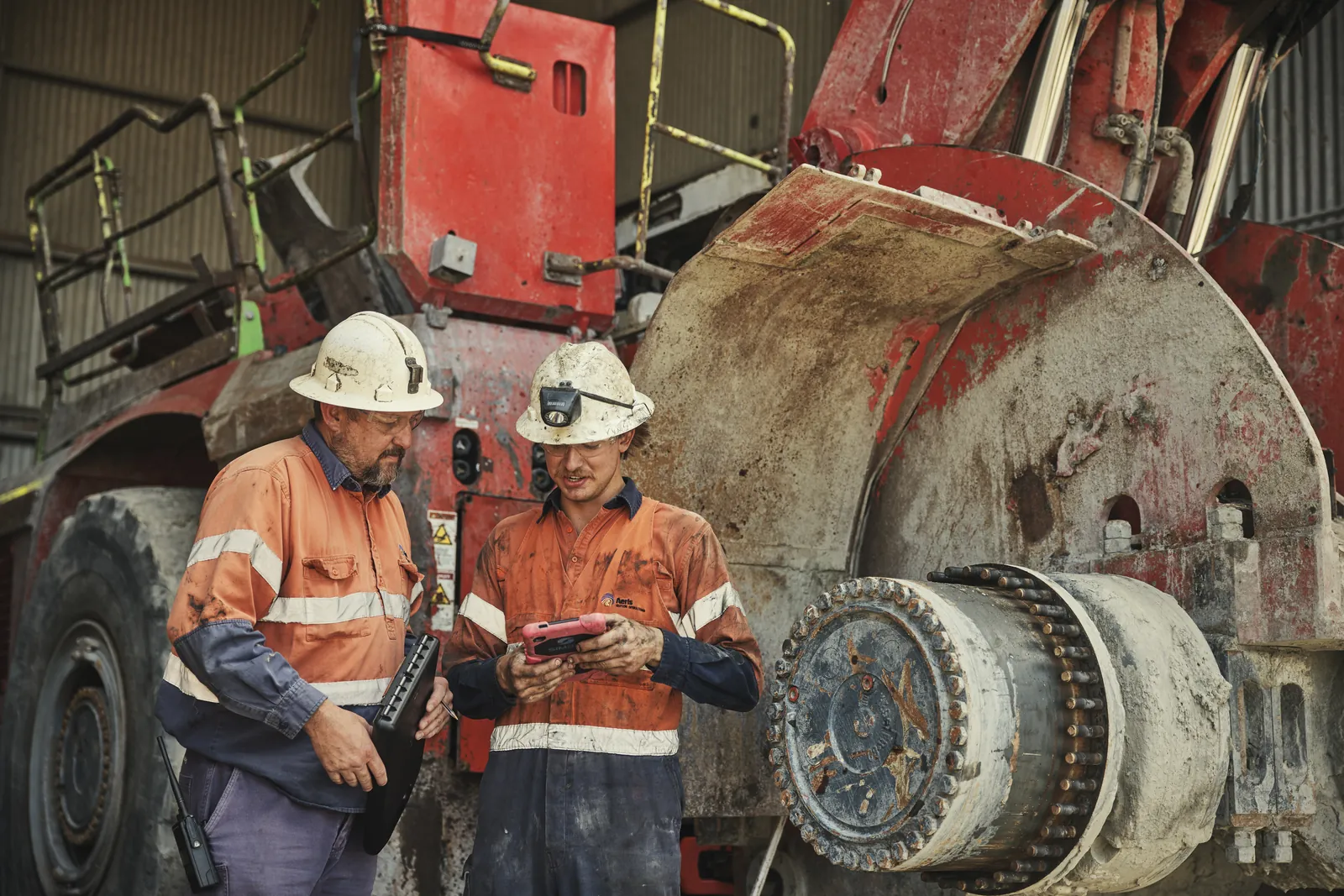 Two Aeris workers check a tablet beside a loader in the workshop