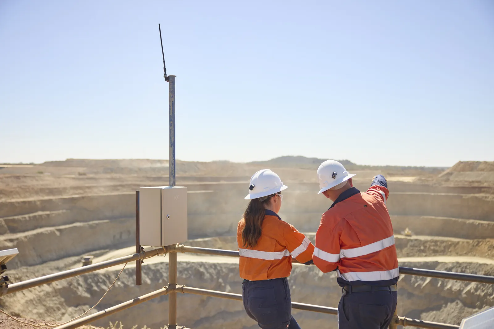 Two Aeris workers look out over an open pit from a viewing platform