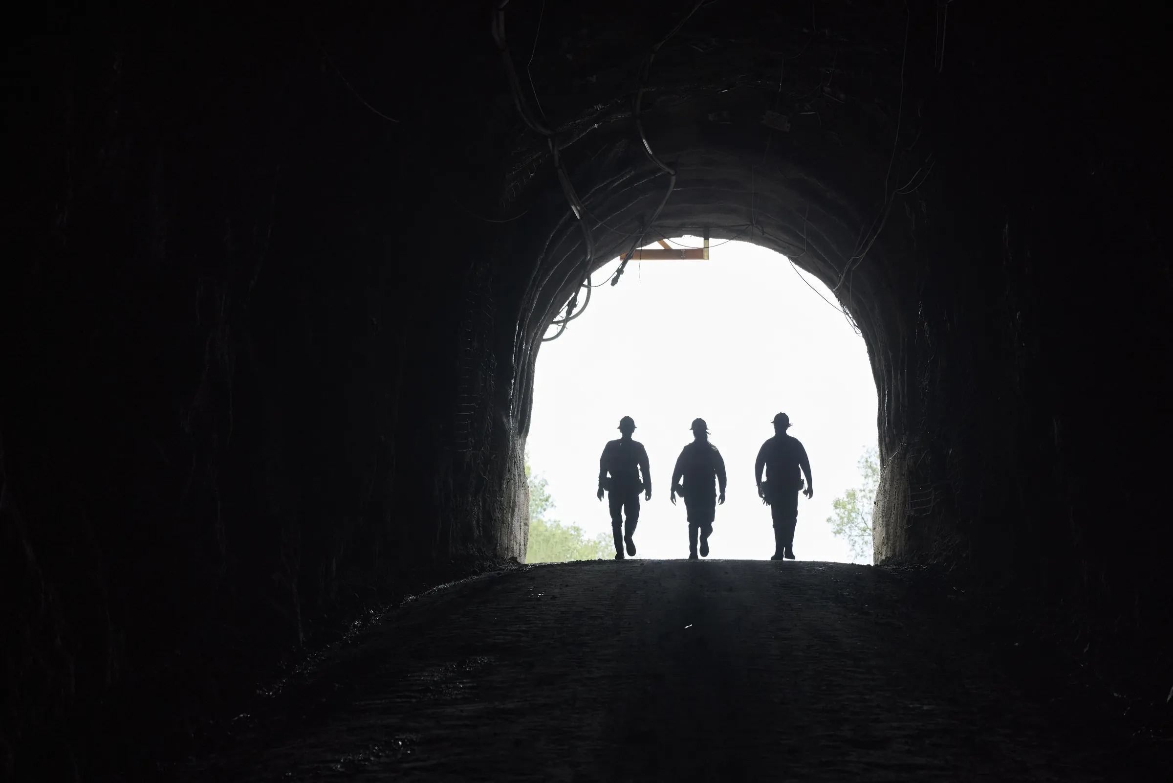 Three workers walking out of an underground portal into daylight
